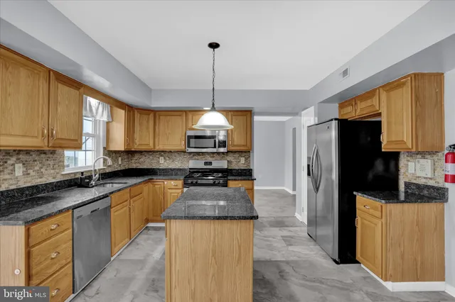 a kitchen with stainless steel appliances granite countertop a refrigerator a sink dishwasher a stove and a dining table with wooden floor