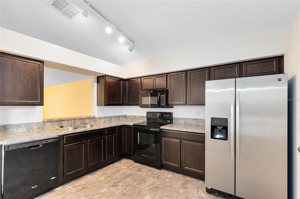 2717 Shelby Ruth Place St. Cloud, FL 34769 - Photo 8 of 31 a kitchen with stainless steel appliances granite countertop a refrigerator a sink a stove a microwave and island with wooden cabinets