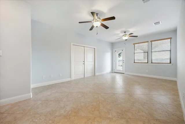 an empty room with chandelier fan and windows
