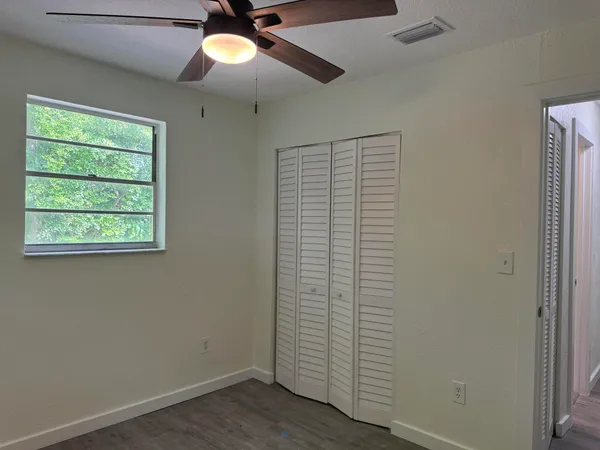 an empty room with wooden floor chandelier fan and windows
