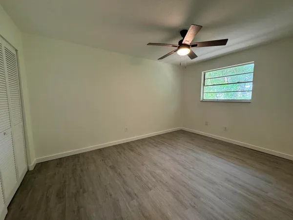 an empty room with wooden floor ceiling fan and windows