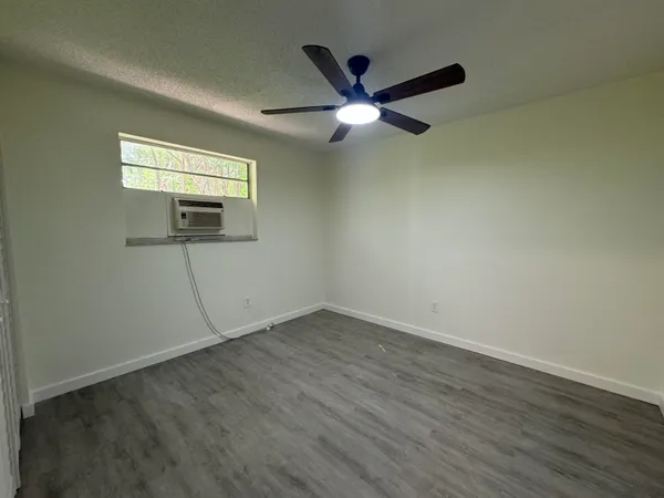 an empty room with wooden floor fan and windows