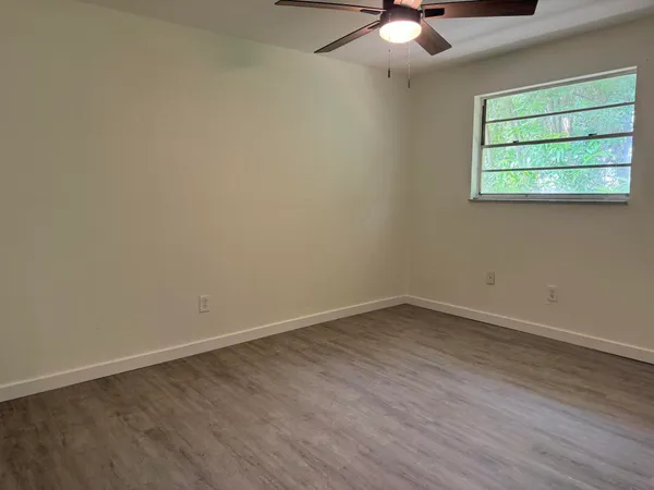 an empty room with wooden floor chandelier fan and windows