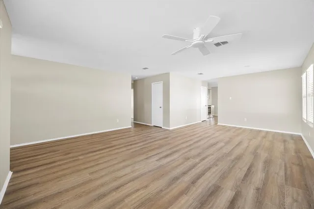 a view of an empty room with wooden floor and a ceiling fan