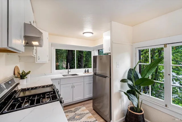 a kitchen with stainless steel appliances a refrigerator a sink a stove a refrigerator white cabinets and wooden floor