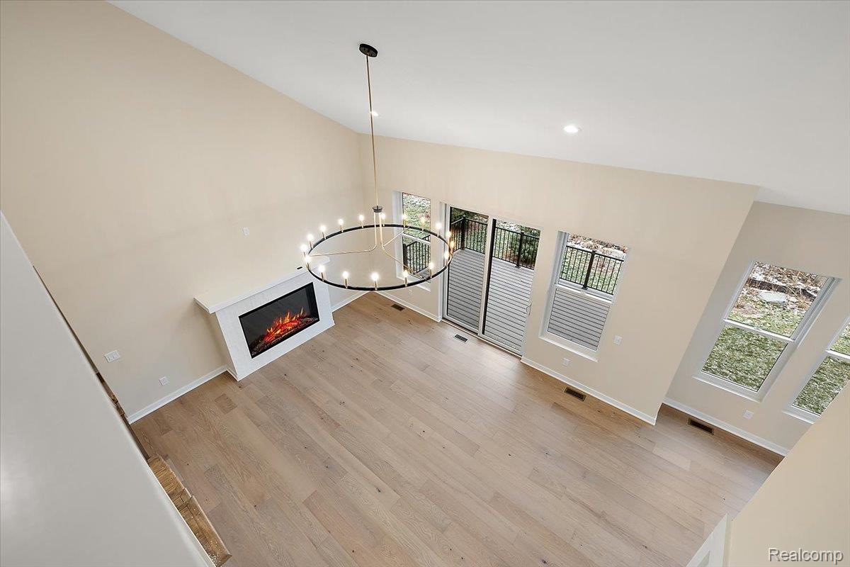 2044 Breckenridge Court Rochester, MI 48309 - Photo 24 of 33 Unfurnished living room with a lit fireplace, light wood-style floors, a chandelier, and a high ceiling