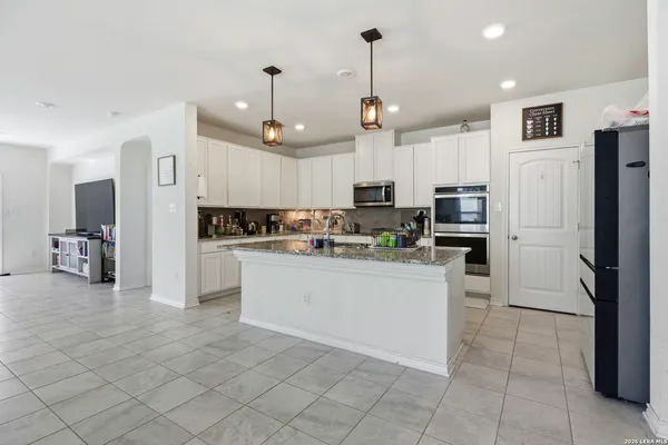 a kitchen with stainless steel appliances kitchen island granite countertop a refrigerator a oven a sink and white cabinets