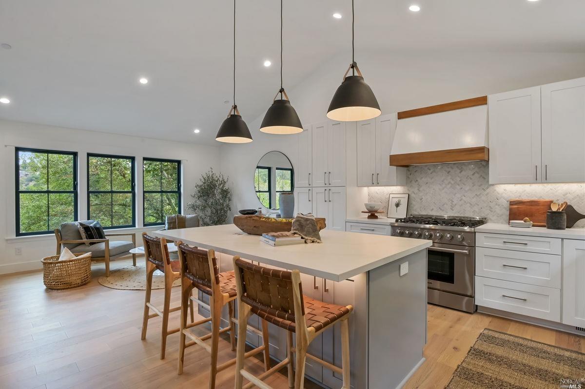 a open kitchen with stainless steel appliances granite countertop a stove a refrigerator a kitchen island a table and chairs