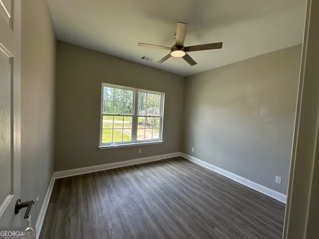 an empty room with wooden floor fan and windows