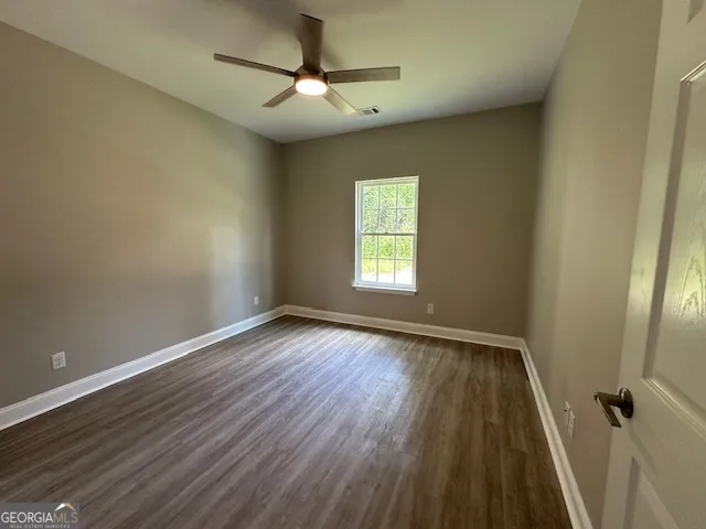 an empty room with wooden floor fan and windows