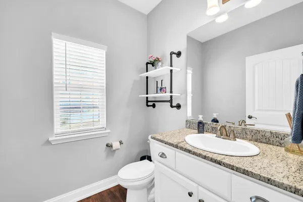 a bathroom with a granite countertop toilet a sink and a window