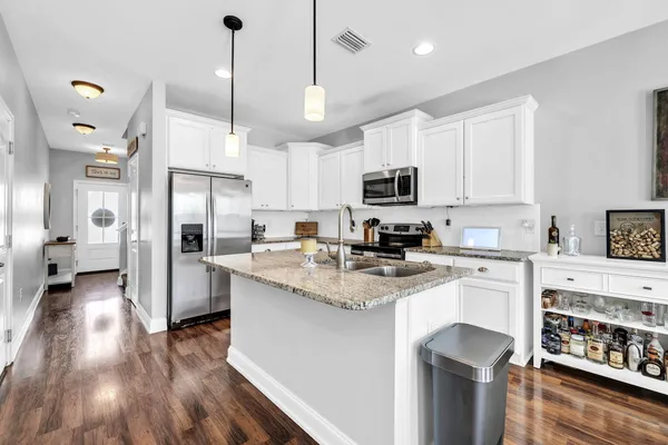 a kitchen with stainless steel appliances granite countertop a refrigerator a stove oven a sink dishwasher and white cabinets with wooden floor