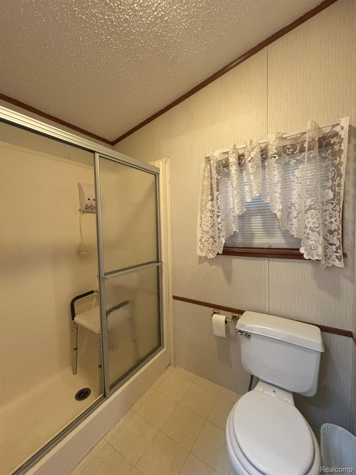 2500 Mann Road Clarkston, MI 48346 - Photo 23 of 28 Full bathroom featuring crown molding, a shower stall, a textured ceiling, light tile patterned flooring, and lofted ceiling