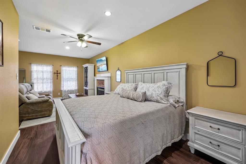 331 Radecke Road Krum, TX 76249 - Photo 33 of 40 Spacious primary bedroom featuring wood-finish flooring, a ceiling fan with integrated lighting, recessed lighting, and a built-in fireplace with a decorative mantel