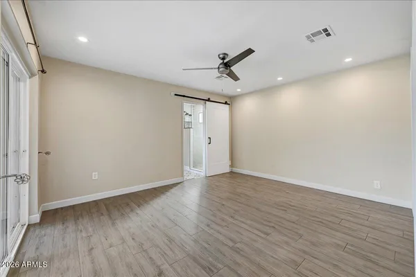 a view of an empty room with wooden floor and a ceiling fan