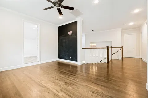 a view of an empty room with wooden floor and a ceiling fan