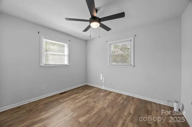 an empty room with wooden floor ceiling fan and windows