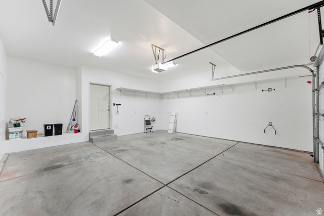 1614 Aspen Loop Provo, UT 84606 - Photo 37 of 47 Spacious garage featuring concrete flooring, ample overhead lighting, built-in wall shelving, an overhead garage door, and an interior access door