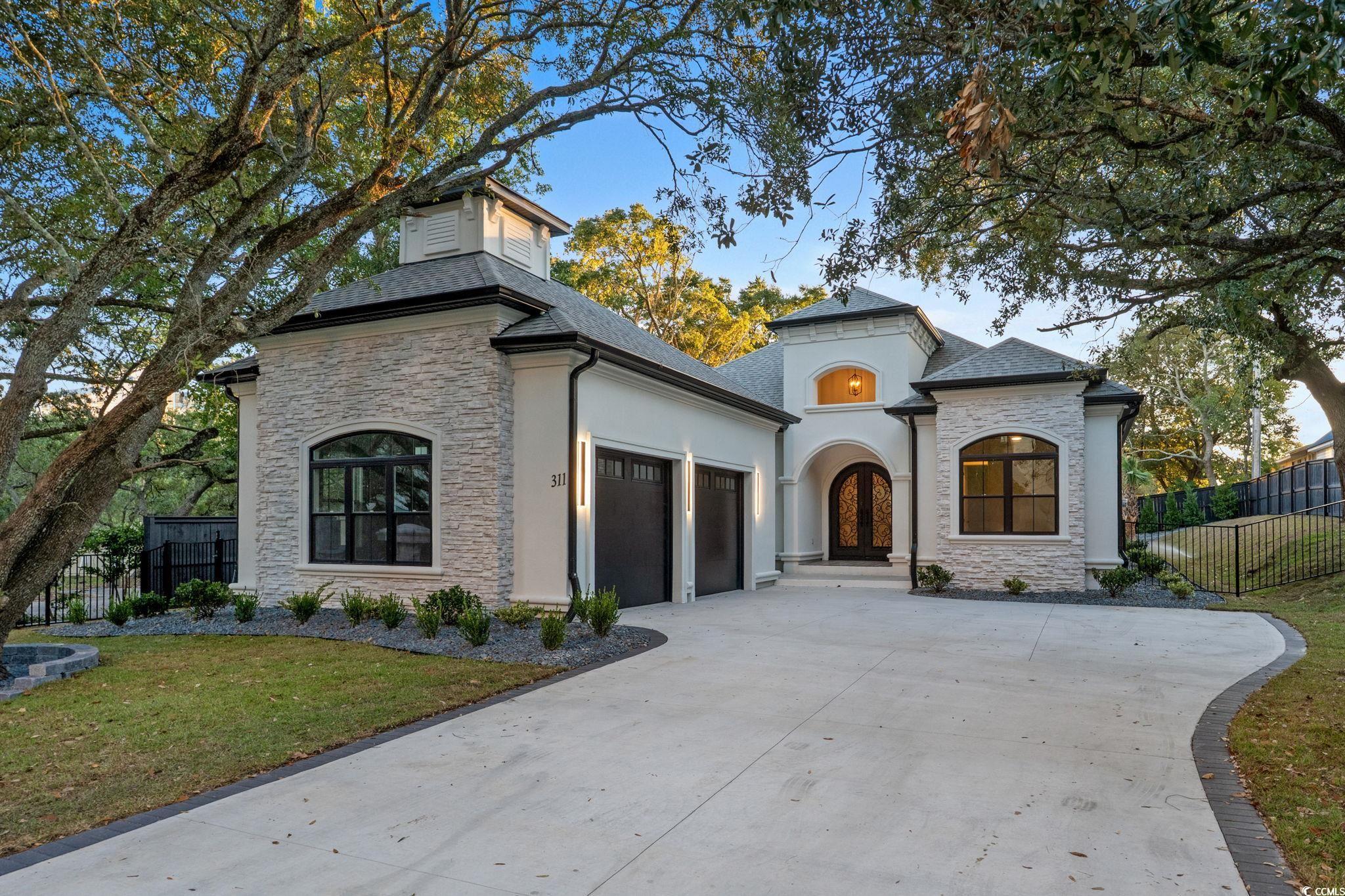 French country home featuring stone siding, a garage, concrete driveway, and stucco siding