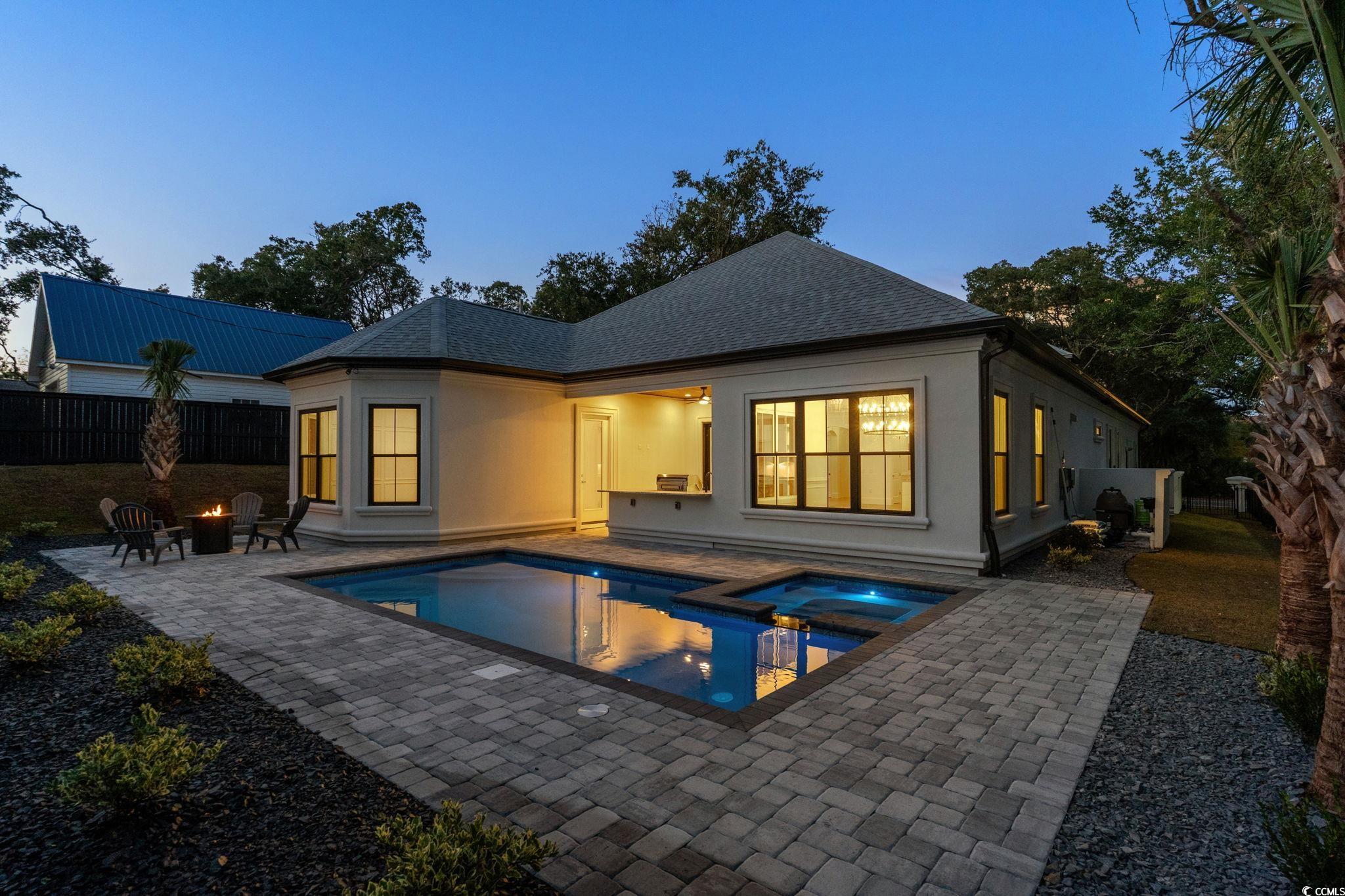 311 73rd Avenue North Myrtle Beach, SC 29572 - Photo 34 of 40 Back of house at dusk featuring an outdoor fire pit, a fenced backyard, a patio, a pool with connected hot tub, and roof with shingles