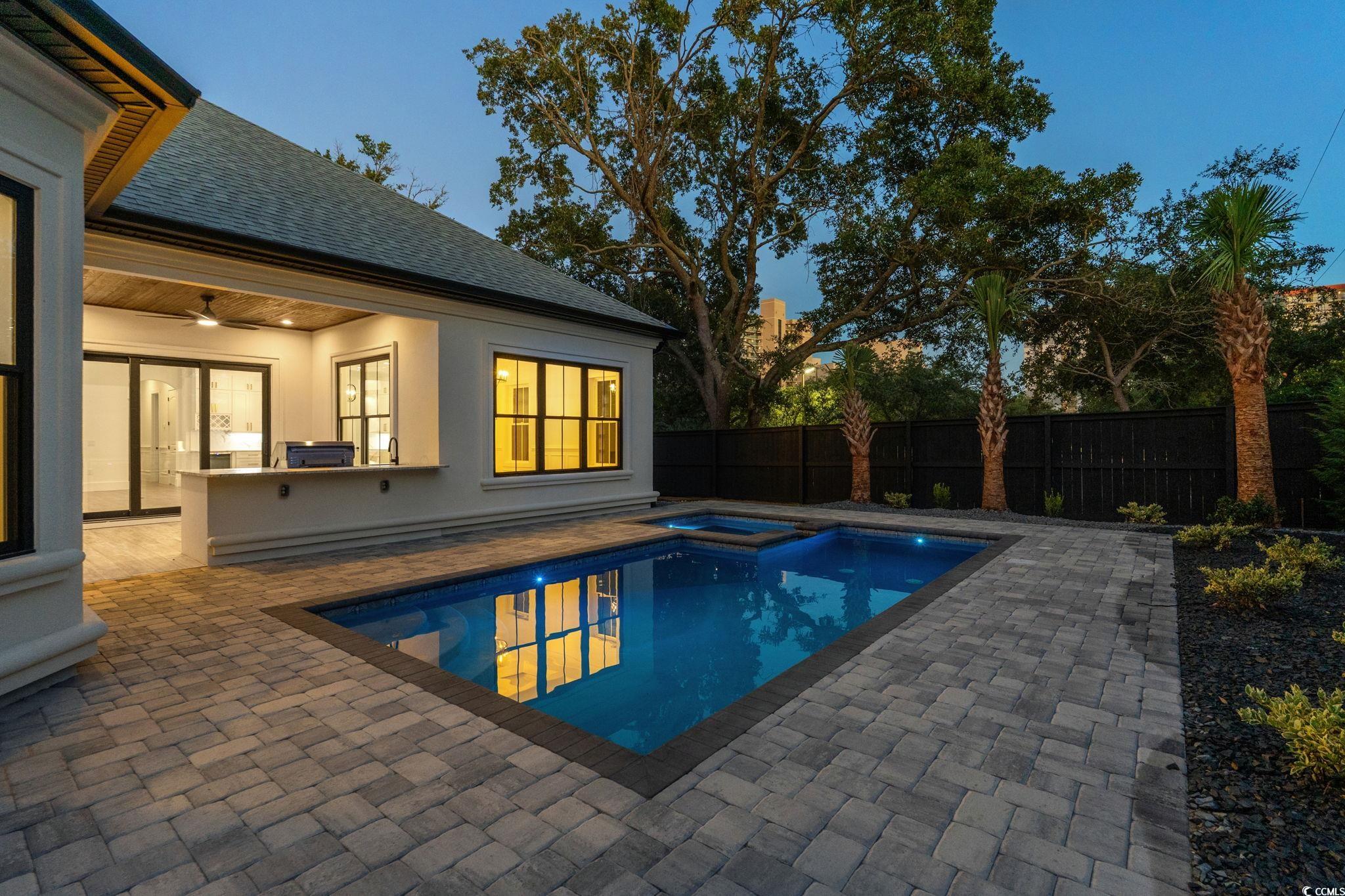 311 73rd Avenue North Myrtle Beach, SC 29572 - Photo 36 of 40 Pool at dusk featuring ceiling fan, exterior kitchen, a fenced backyard, a patio area, and a pool with connected hot tub
