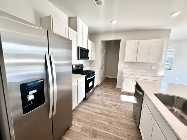 a kitchen with stainless steel appliances kitchen island granite countertop a refrigerator a stove and a sink with wooden floor