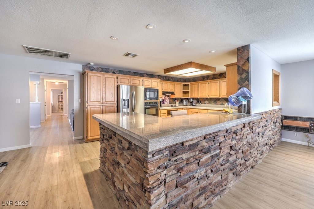 2240 Grayson Circle Henderson, NV 89014 - Photo 15 of 38 Kitchen with black appliances, a peninsula, a textured ceiling, backsplash, and light wood-type flooring