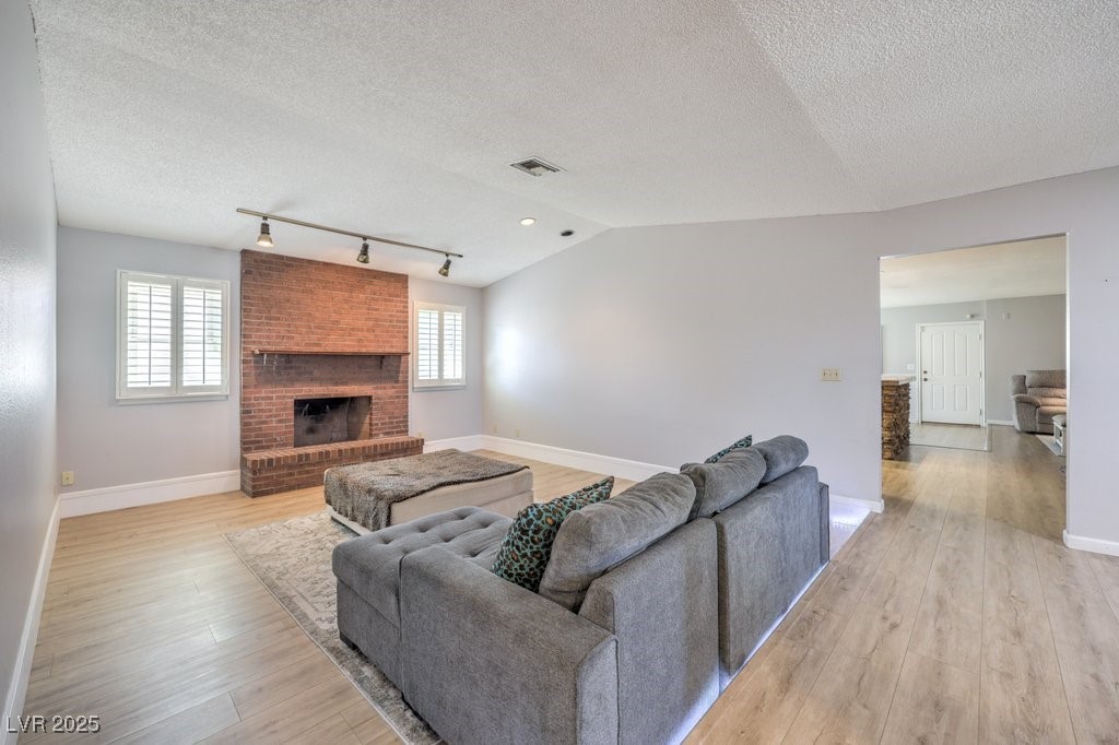 2240 Grayson Circle Henderson, NV 89014 - Photo 8 of 38 Living room featuring light wood-type flooring, rail lighting, a brick fireplace, a textured ceiling, and lofted ceiling