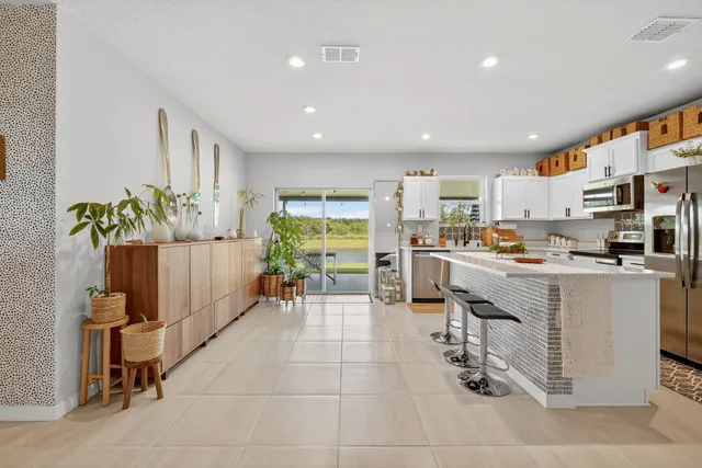 a kitchen with stainless steel appliances kitchen island granite countertop dining table chairs and a refrigerator