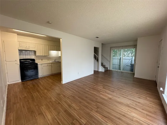 an empty room with wooden floor kitchen view and windows