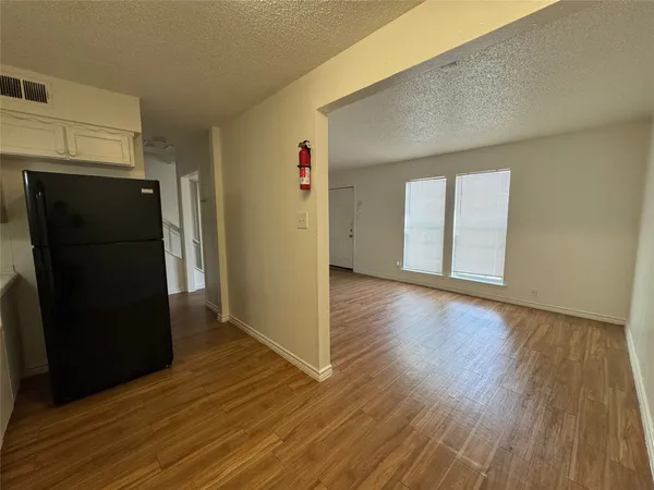 a view of a refrigerator in kitchen and an empty room with wooden floor and a window