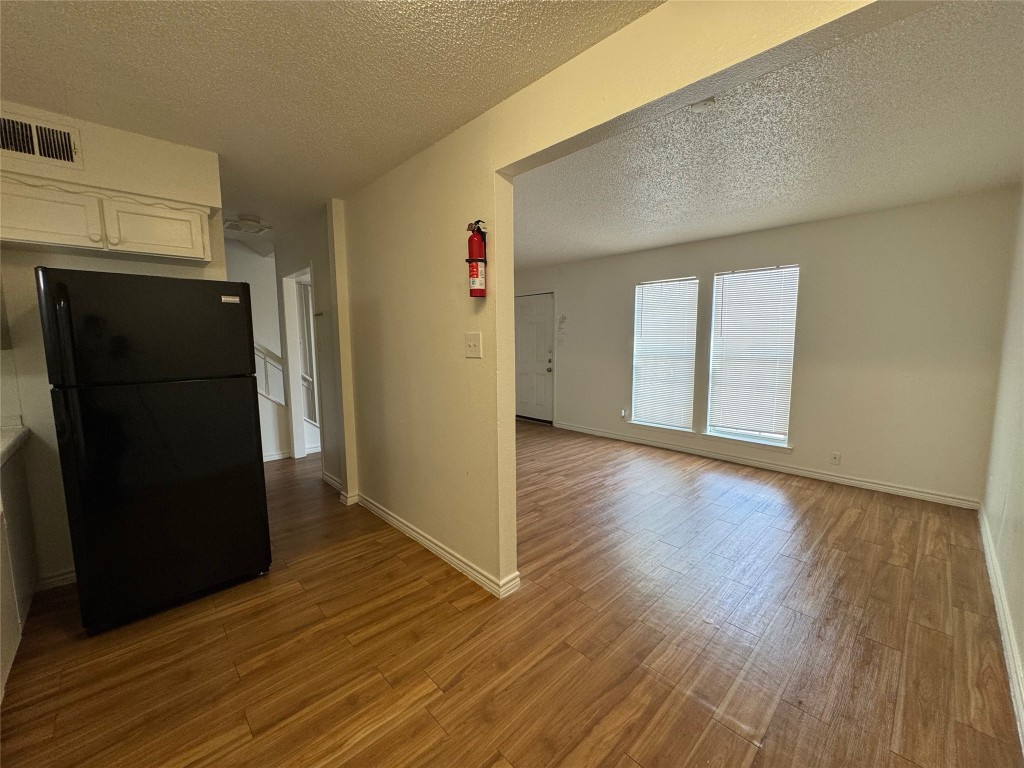 4810 West Wind Trail, Unit 101 Austin, TX 78745 - Photo 7 of 21 a view of a refrigerator in kitchen and an empty room with wooden floor and a window