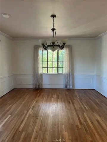 an empty room with wooden floor chandelier and windows