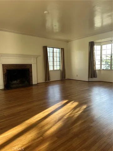 an empty room with wooden floor fireplace and windows