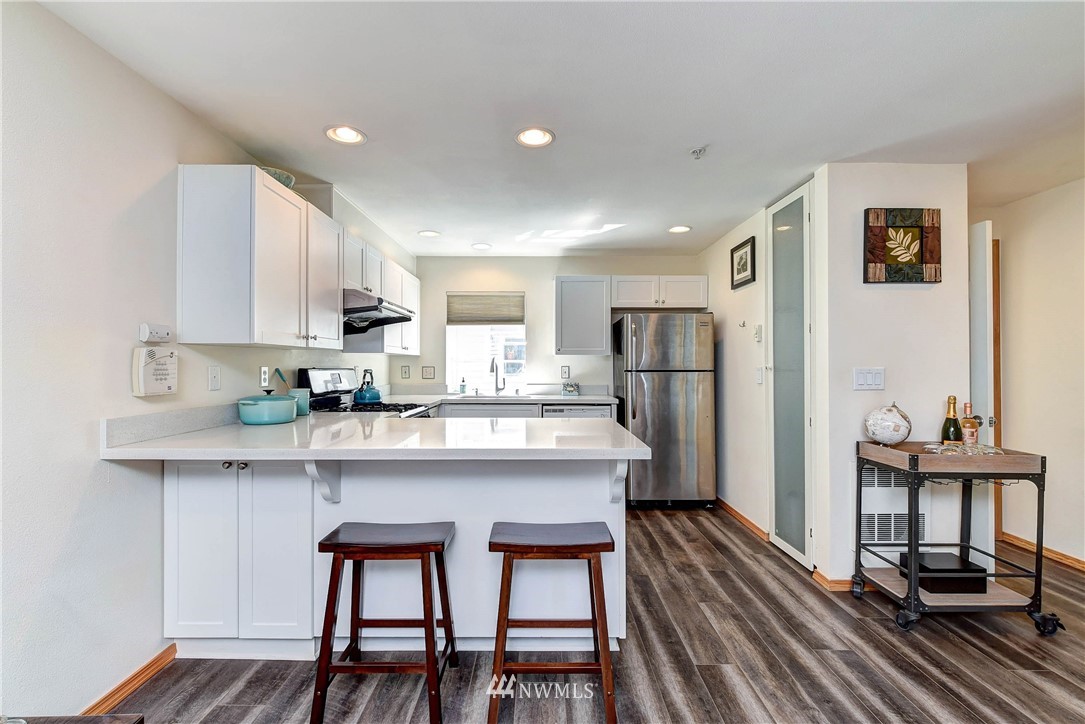 1311 North 145th Street, Unit B Seattle, WA 98133 - Photo 2 of 31 a kitchen with stainless steel appliances a dining table chairs refrigerator and sink