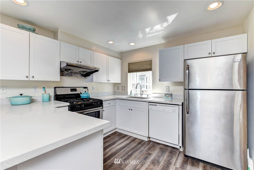 1311 North 145th Street, Unit B Seattle, WA 98133 - Photo 5 of 31 a kitchen with granite countertop a refrigerator a sink dishwasher a stove top oven a refrigerator and white cabinets with wooden floor
