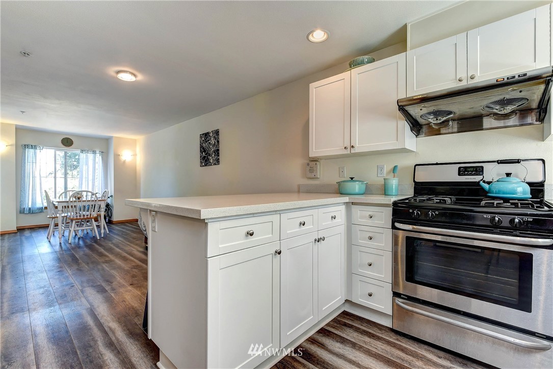 1311 North 145th Street, Unit B Seattle, WA 98133 - Photo 6 of 31 a kitchen with stainless steel appliances a stove a sink cabinets and wooden floor