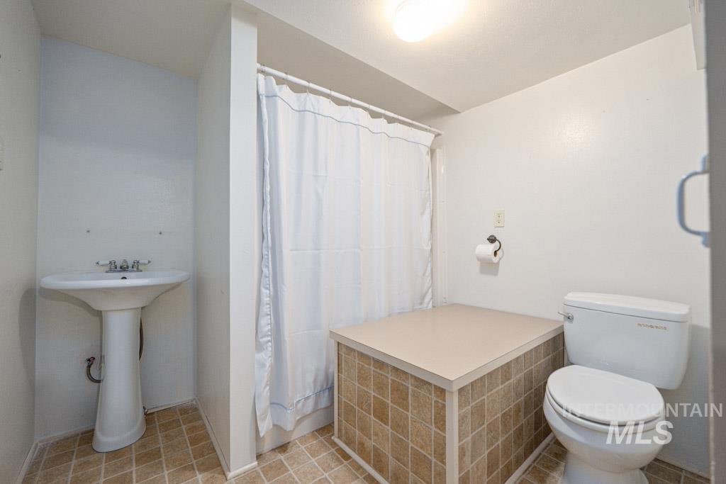 259 Highway 12 Pomeroy, WA 99347 - Photo 32 of 45 Bathroom featuring a pedestal sink, white toilet, and a shower with a tiled base and shower curtain