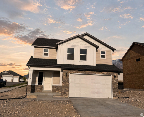 View of front of home with driveway, covered porch, a garage, stone siding, and board and batten siding