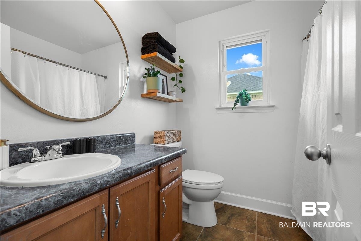 8952 Sherman Road Foley, AL 36535 - Photo 21 of 41 Bathroom featuring a single-sink vanity with wood-finish cabinetry, a framed mirror, a window, and tile flooring