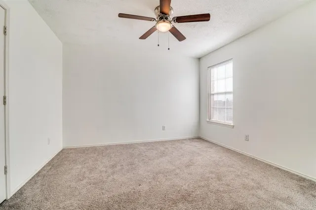 an empty room with chandelier fan and windows