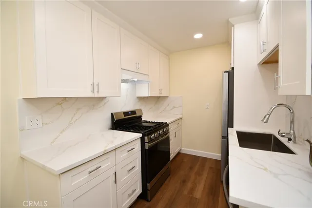 a kitchen with stainless steel appliances granite countertop a sink stove and white cabinets with wooden floor