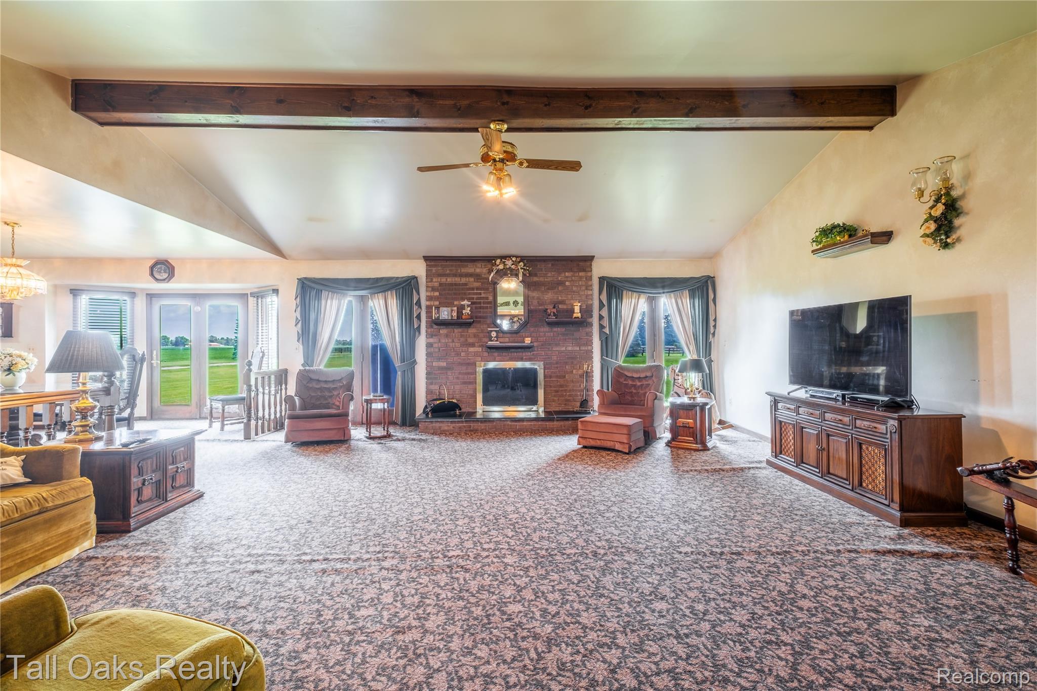 79330 Capac Road Armada, MI 48005 - Photo 27 of 42 Spacious living area featuring a vaulted ceiling with exposed wood beams, a brick fireplace, and double French doors opening to an exterior landscape