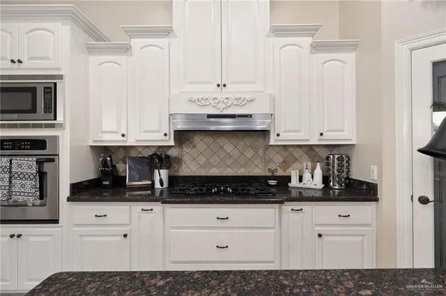 a white kitchen with granite countertop white cabinets and stainless steel appliances