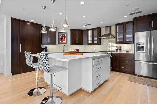 a kitchen with stainless steel appliances kitchen island granite countertop a refrigerator a stove a sink and a dining table with wooden floor