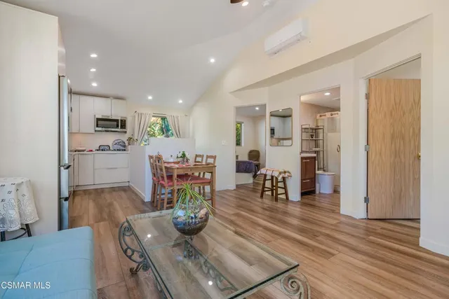 a living room with stainless steel appliances furniture wooden floor and a kitchen view