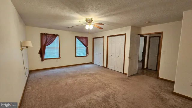 an empty room with chandelier fan and windows