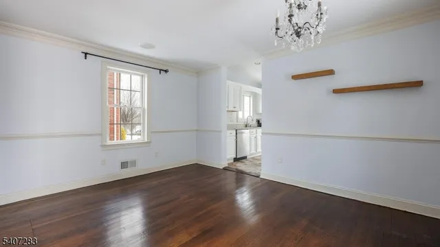 an empty room with wooden floor chandelier and windows