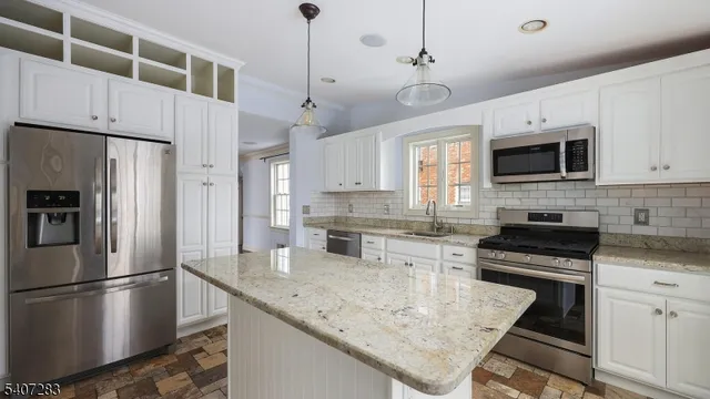 a kitchen with stainless steel appliances granite countertop a refrigerator a stove a microwave oven a sink a stove and white cabinets