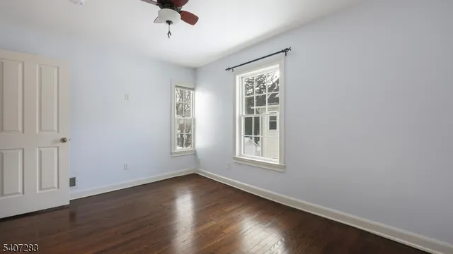 an empty room with wooden floor chandelier fan and windows